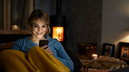 Frau schaut unter der Bettdecke auf ihren Smartphone-Bildschirm